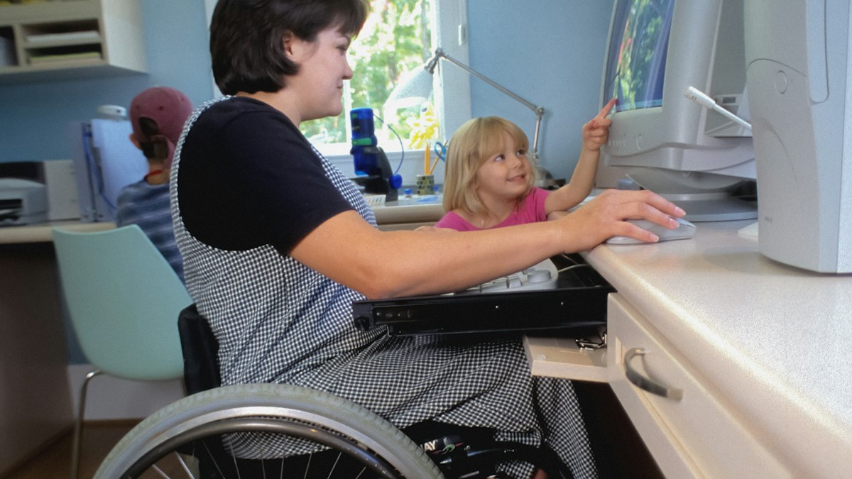 A woman using a wheelchair works at a computer at an adapted desk