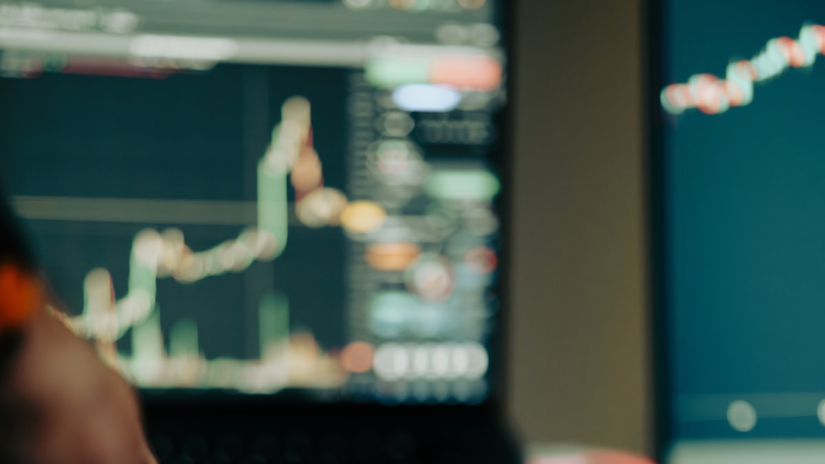 A person pointing at a chart on a laptop screen while reviewing the numbers at a desk