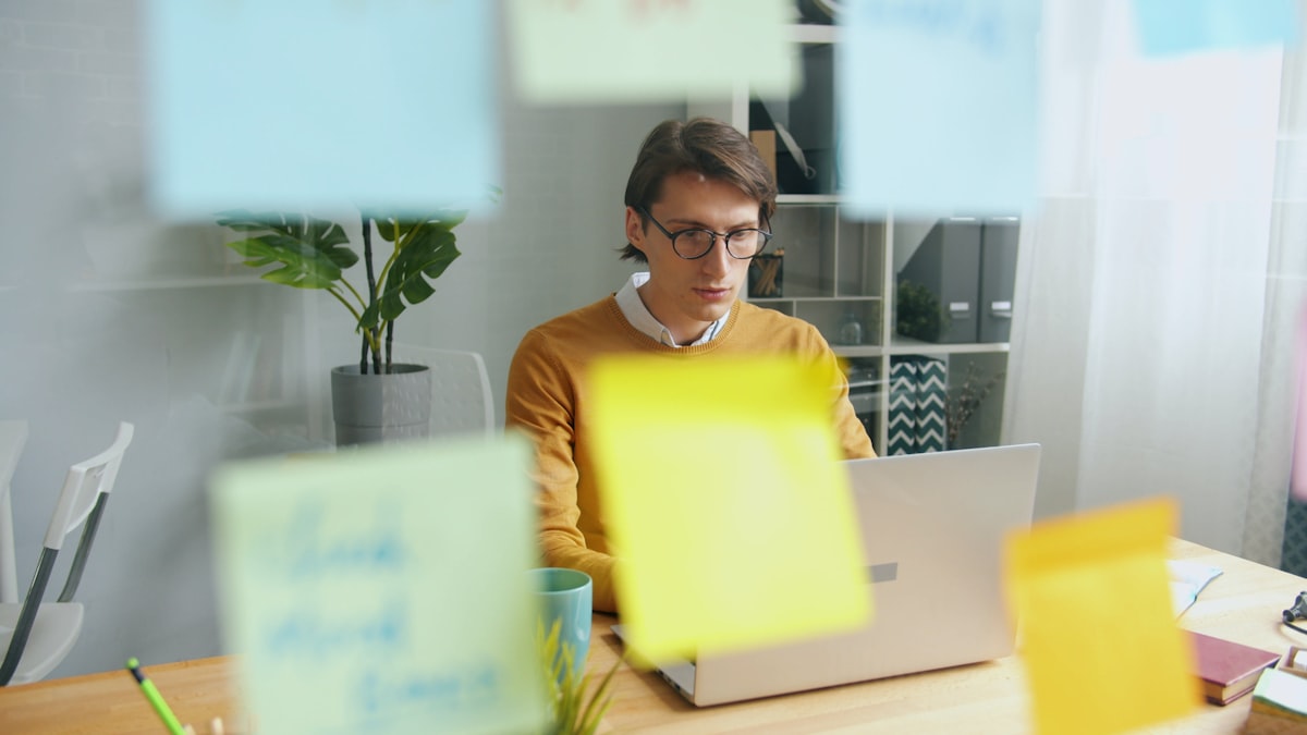 A person working on a laptop at a desk surrounded by colorful sticky notes mapping out a decision process