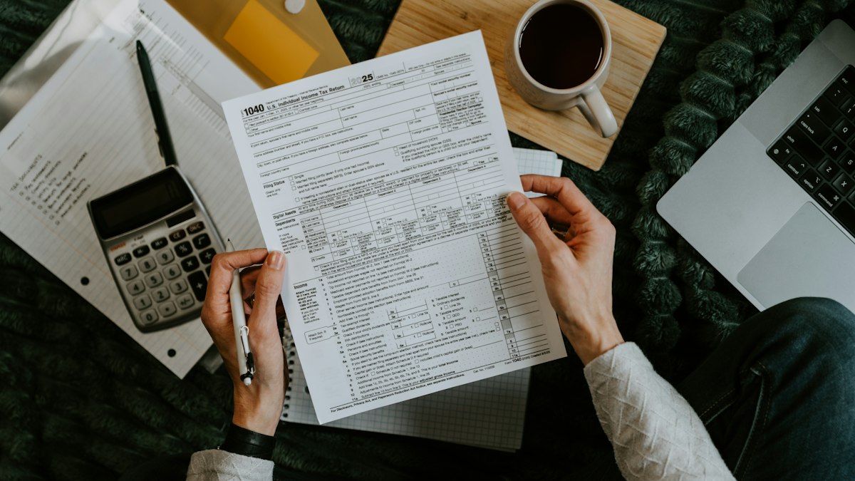 Hands holding financial paperwork next to a calculator and open laptop on a desk