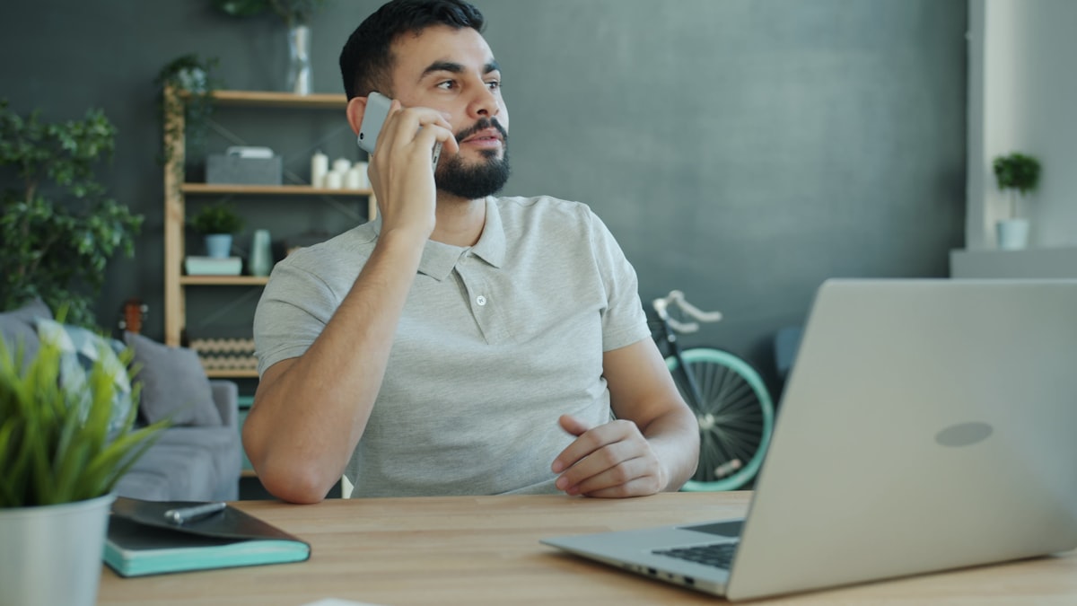 A real estate agent on a phone call at a desk with a laptop open to a property listing