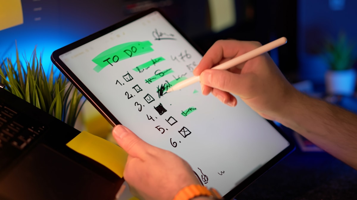 A hand holding a stylus checking off items on a digital to-do list on a tablet