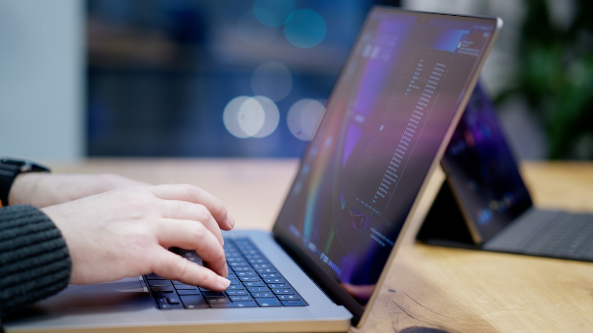 A person typing on a laptop keyboard at an office desk, drafting a document