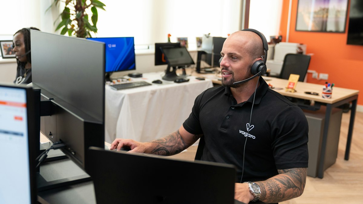A person wearing a headset working at a desktop computer during a phone call