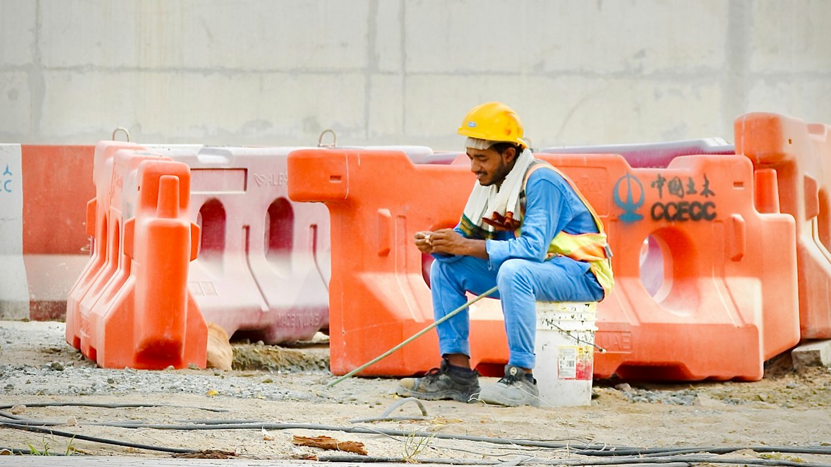 A technician in a hard hat and safety vest sits at a job site using his mobile phone