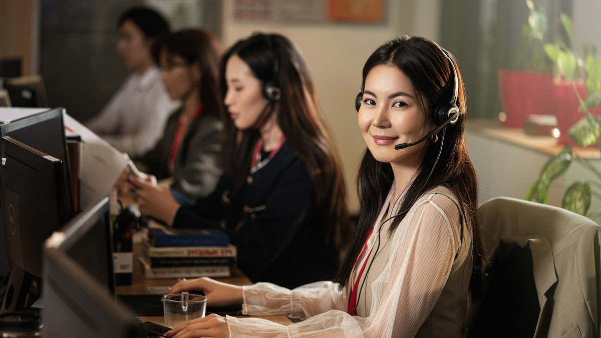 A smiling receptionist wearing a headset answers calls at a front desk computer