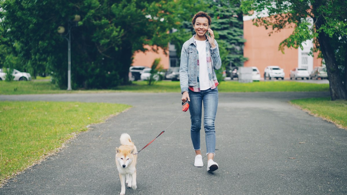 A woman talking on her phone outdoors while walking her dog on a leash