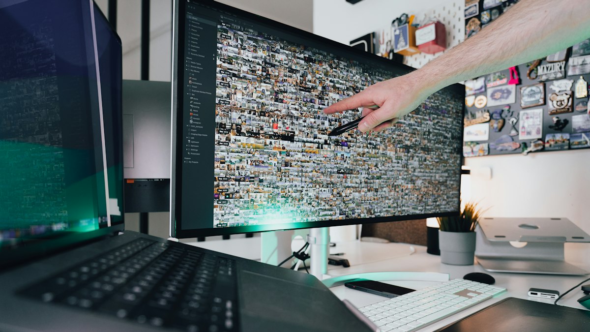 A person at a desk pointing at a monitor showing colorful bar and line charts on a marketing dashboard