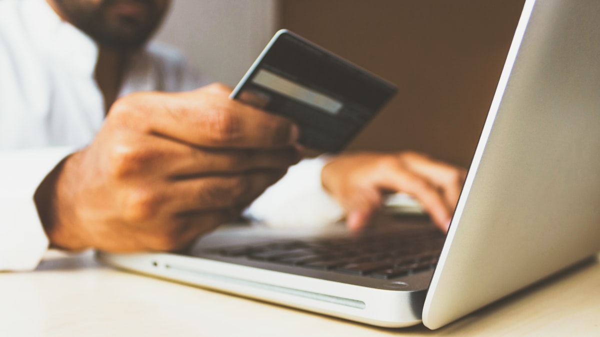 A person at a laptop holding a payment card during an online checkout