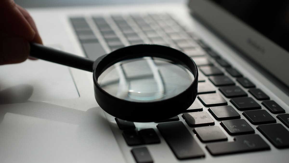 A hand holds a magnifying glass over a laptop keyboard, representing the process of searching through a company's own documents